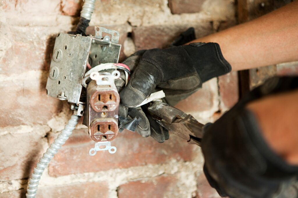 An electrician works on wiring an outlet against a brick wall
