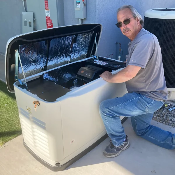 Bruce Goodkin Electric A man kneels beside an open standby generator outdoors, inspecting its control panel next to an air conditioning unit.