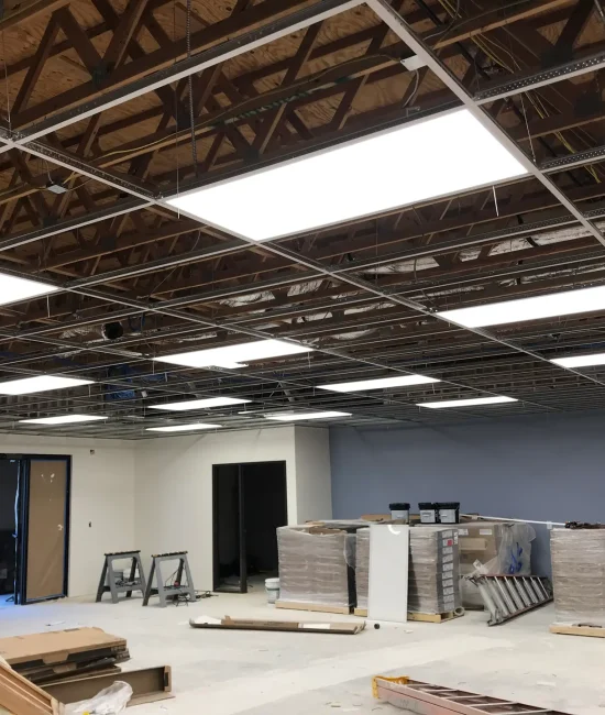 Goodkin (9) Office under renovation with exposed ceiling, LED panel lights installed, construction materials, and equipment scattered on the floor.